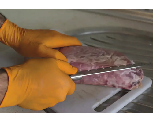 O persoană cu mănuși taie carne cu un cuțit pe un tocător.