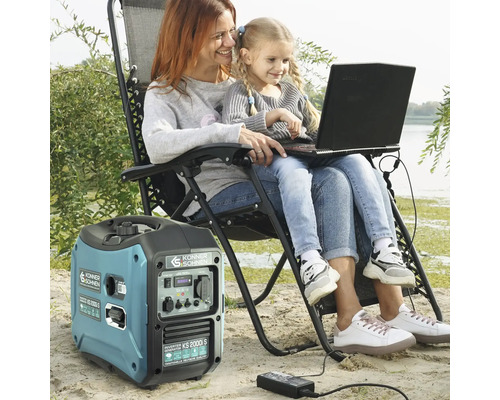 Mamă și fiică folosind un laptop alimentat de un generator electric portabil pe o suprafață nisipoasă.