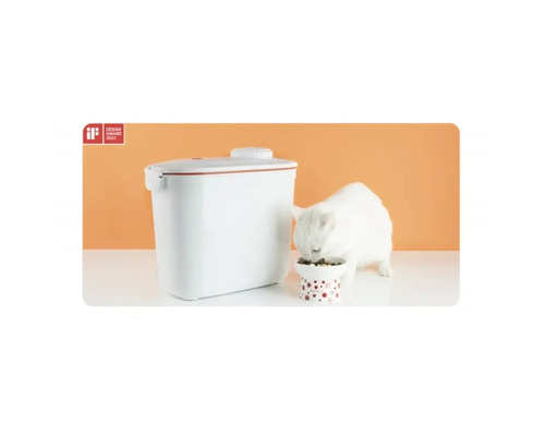 Distribuitor automat de hrană pentru pisici lângă o pisică care mănâncă.