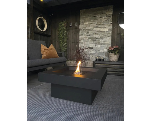 Spațiu exterior întunecat cu canapea, decor din piatră și masă de foc cu etanol