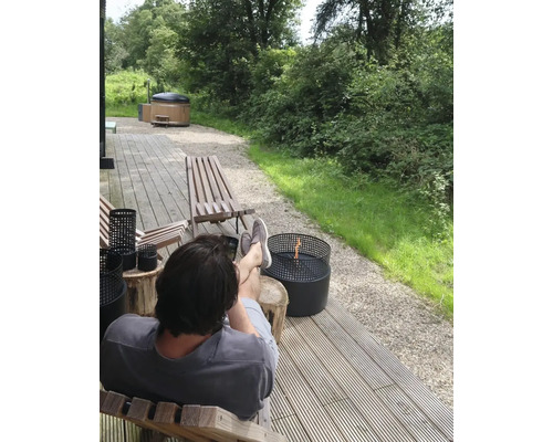 Bărbat relaxându-se pe o terasă cu o cadă cu hidromasaj și un vas de foc în aer liber.