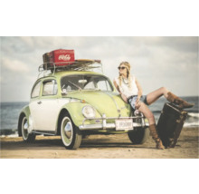 O femeie se sprijină de un Volkswagen Beetle de epocă cu suport de bagaje și bagaje în fața unei mări.