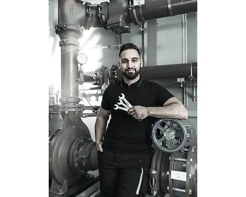 Un instalator cu chei stă în fața unui sistem de pompare industrial.