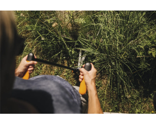 Persoană care taie iarba cu o foarfecă manuală de tuns iarba.