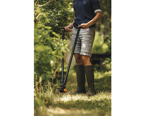 O persoană ține o foarfecă de iarbă cu mâner lung în grădină.