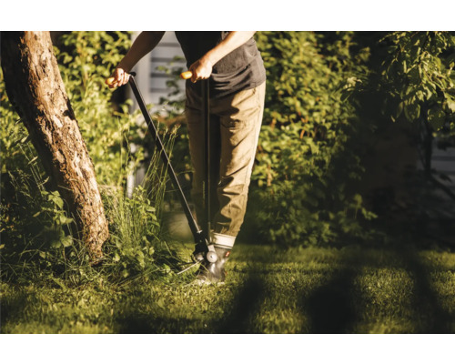 O persoană folosește o foarfecă de iarbă manuală în grădină pentru tunderea precisă a marginilor gazonului.