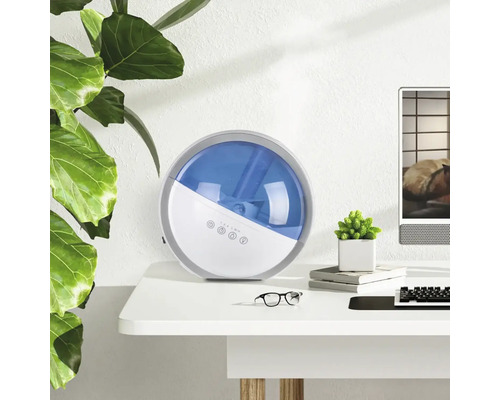 Umidificator pe un birou lângă o plantă de apartament și un computer