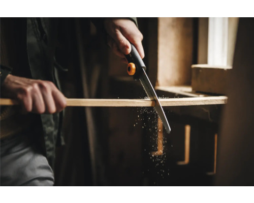 O persoană taie o scândură de lemn cu un ferăstrău manual.