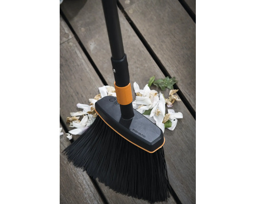 Mătură Fiskars cu mâner și resturi de flori pe podea de lemn