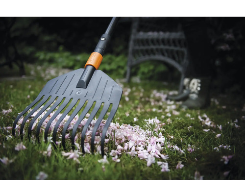 Greblă de grădină măturând petale de flori pe gazon