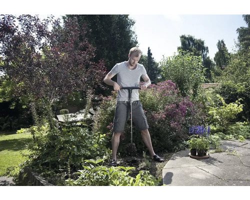 Un bărbat folosește un burghiu de pământ în grădină pentru a face găuri.