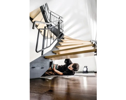 Bărbat care montează o scară spiralată cu o șurubelniță electrică și o lampă de lucru
