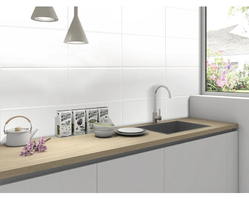 Bucătărie luminoasă cu chiuvetă, robinet, veselă și ceai de plante în fața faianței albe