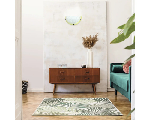 Cameră de zi cu lampă de perete, comodă, covor și canapea verde pentru o atmosferă luminoasă și organizată.