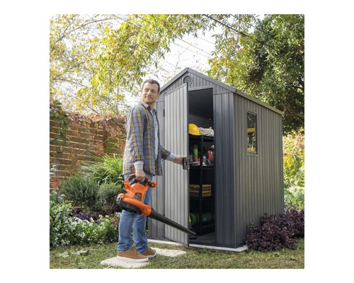 Scenă de grădină cu un bărbat ținând o suflantă de frunze și deschizând o magazie de grădină cu rafturi și unelte de grădină.