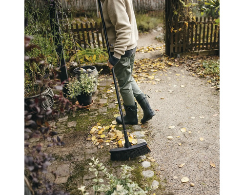 Persoană mătură frunzele cu o mătură de stradă în grădină.