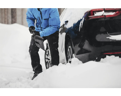 Persoană care curăță zăpada lângă o mașină.