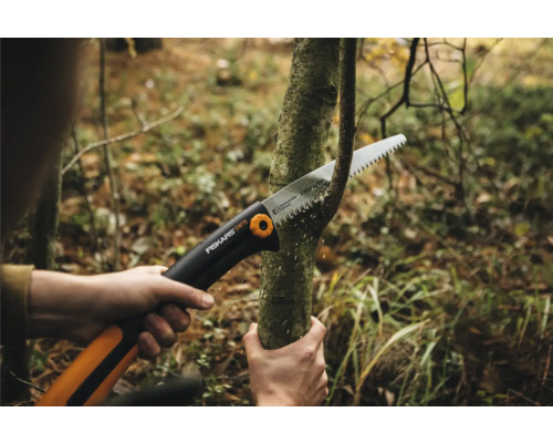 O persoană taie o ramură cu un ferăstrău de mână.