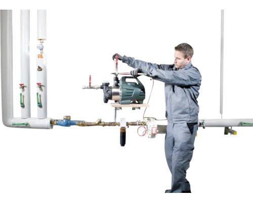 Un instalator montează o pompă de grădină la un sistem de conducte.