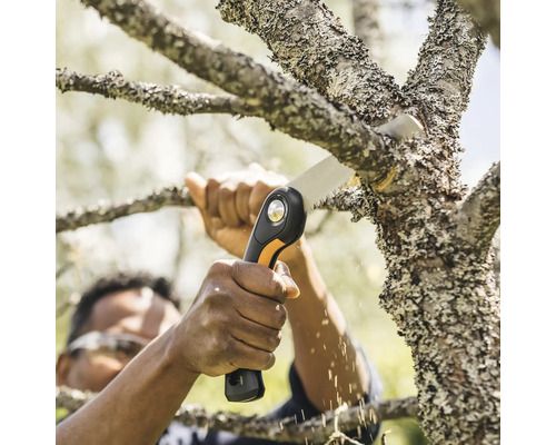 O persoană taie o ramură cu un fierăstrău de mână.