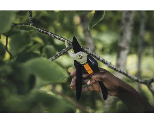 O mână taie o ramură cu o foarfecă de grădină Fiskars.