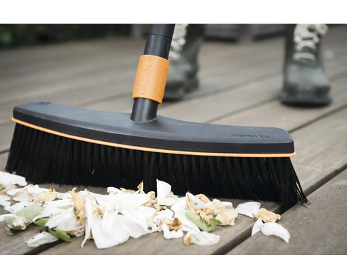 Mătură pentru curățarea unei terase din lemn cu resturi de plante.