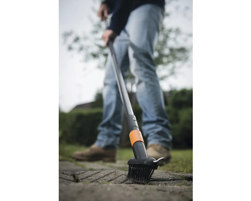 Un bărbat folosește o perie pentru rosturi pentru a îndepărta buruienile dintre pietrele de pavaj.