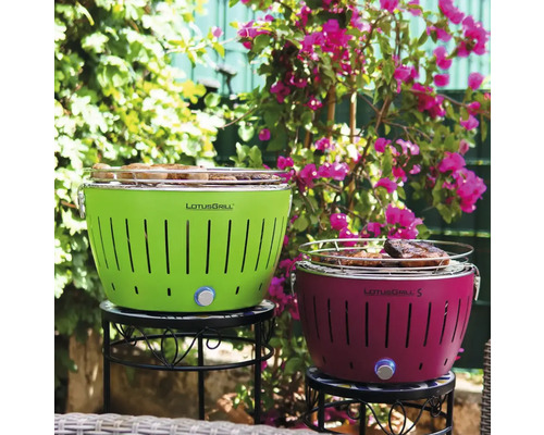 Două grătare LotusGrill pe o masă în fața unor plante cu flori.