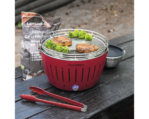 Grătar cu cărbune Lotusgrill cu alimente la grătar, clește de grătar și cărbune pe o masă