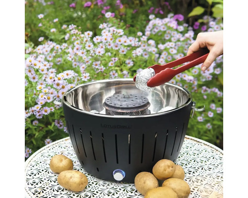 Grătar LotusGrill cu clește de grătar și cartofi pe o masă în grădină