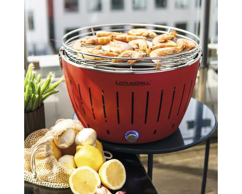 Grătar LotusGrill roșu cu creveți pe grătar, împreună cu lămâie și usturoi pe o masă.