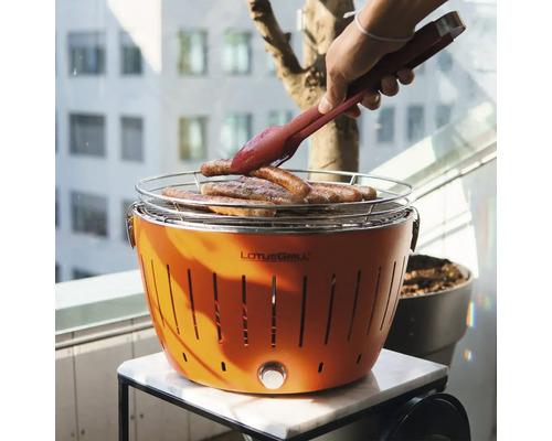 Grătar LotusGrill portocaliu cu alimente la grătar și clește pe o masă