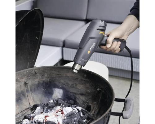 O persoană aprinde cărbune de grătar cu un pistol cu aer cald Steinel.