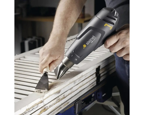 Mesterșugarul îndepărtează vopseaua de pe o ușă de lemn cu un pistol cu aer cald și o spatulă