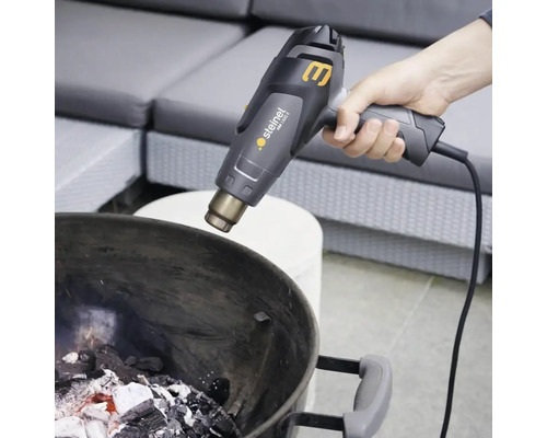 O persoană aprinde cărbuni de lemn într-un grătar cu un pistol cu aer cald.