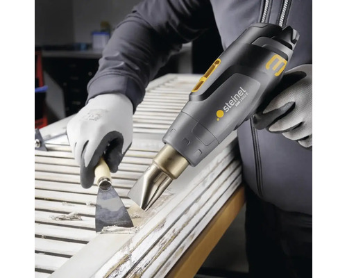 O persoană îndepărtează vopseaua de pe o ușă cu un pistol cu aer cald și o spatulă.