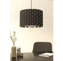 Lampa suspendată cu abajur negru și model împletit deasupra unei mese de sufragerie.