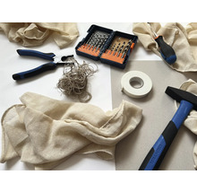 Diverse unelte și materiale, inclusiv un ciocan, clește, șurubelniță, burghie, bandă adezivă și material textil