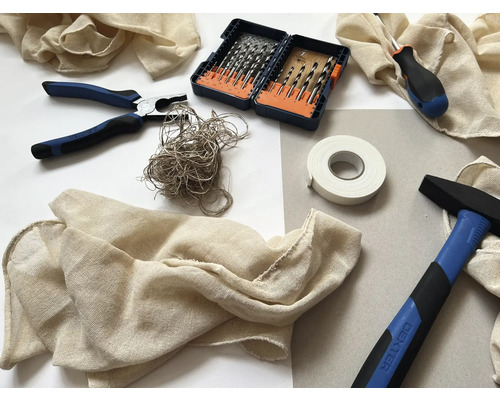 Diverse unelte și materiale, inclusiv un ciocan, clește, șurubelniță, burghie, bandă adezivă și material textil