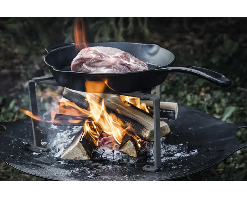 Carne este preparată într-o tigaie deasupra unui foc de tabără