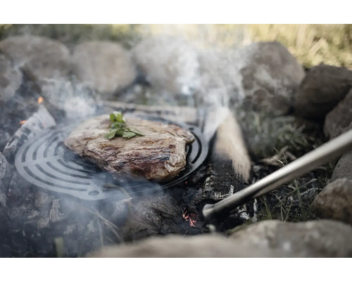 Friptură pe grătar deasupra unui foc deschis cu pietre.