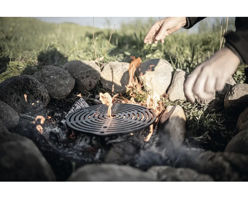 Loc de foc cu grătar, înconjurat de pietre, cu mâini deasupra