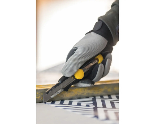 O mână într-o mănușă de lucru folosește un cuțit pentru a tăia material.