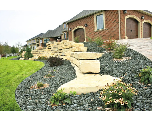 Exterior cu zid de piatră naturală, pietriș și plantare în fața casei