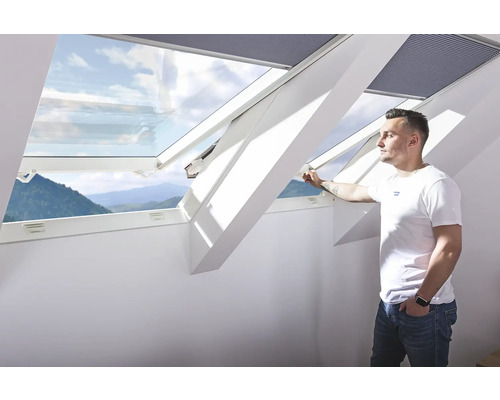 Bărbat deschizând o fereastră de mansardă cu vedere spre exterior