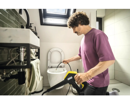 Un bărbat curăță toaleta cu un curățător cu presiune Kärcher în baie.