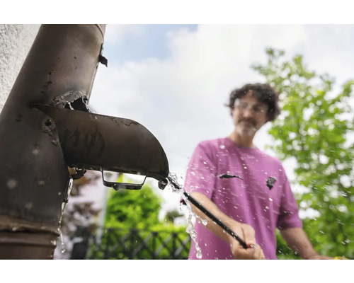 Un bărbat curăță un jgheab înfundat cu o unealtă.