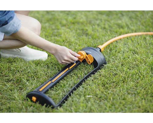 O persoană ajustează un aspersor de gazon Fiskars pe un gazon.