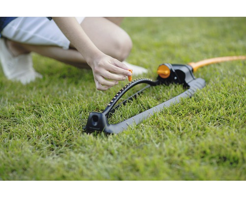 O persoană reglează un regulator pe un aspersor de gazon care stă pe un gazon.