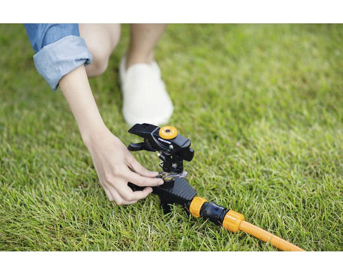 O persoană reglează un aspersor de gazon pe gazon.